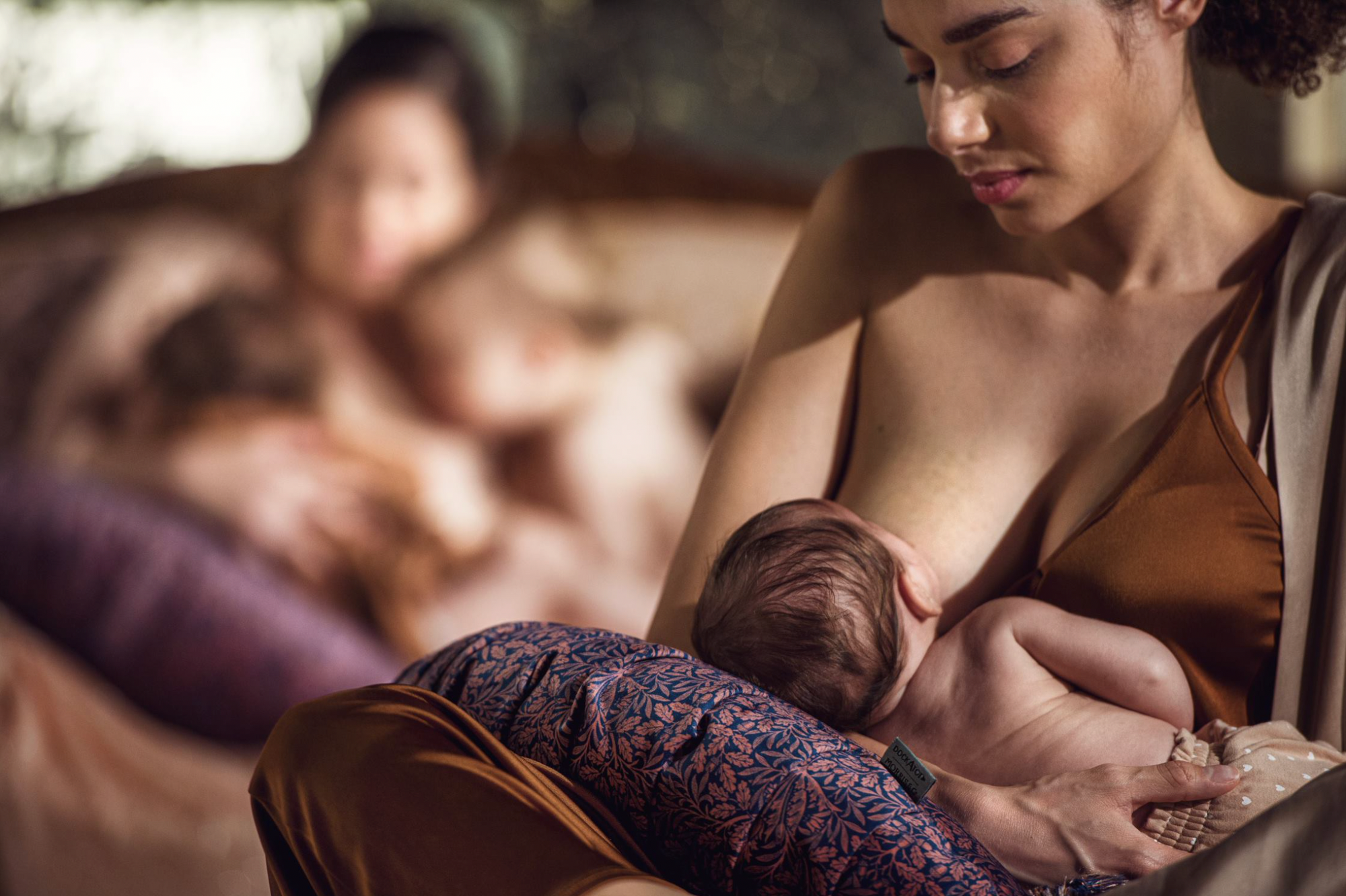 Mother breastfeeding baby using a DockATot nursing pillow in Acorn print